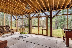 A spacious room with a wooden ceiling, large windows, a bench, a chair, and a foosball table.