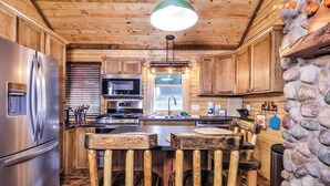 Una cucina rustica con armadietti in legno, un frigorifero in acciaio inox, una parete decorata con pietra e un'isola centrale con sgabelli.
