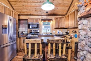 Eine rustikale Küche mit Holzschränken, einem Edelstahlkühlschrank, einer Wand mit Steinverkleidung und einer zentralen Kochinsel mit Barhocker.