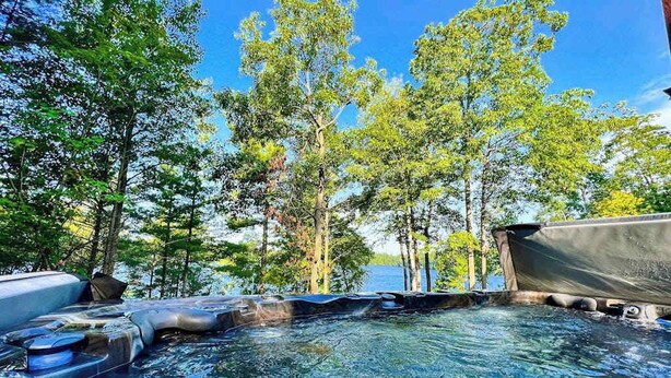 A hot tub surrounded by trees and a body of water. - 3-story chalet with private hot tub, game room & waters toys - dog-friendly (Lac Du Flambeau)