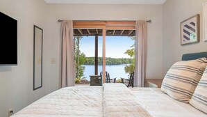 A bedroom with a bed, a TV, a view of a lake, and a chair outside. - 3-story chalet with private hot tub, game room & waters toys - dog-friendly (Lac Du Flambeau)