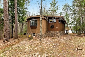A rustic cabin with a stone foundation, a wooden exterior, and a small porch. - Cozy lakefront cabin in the heart of Wisconsin's Northwoods with canoe & kayak (Lac Du Flambeau)