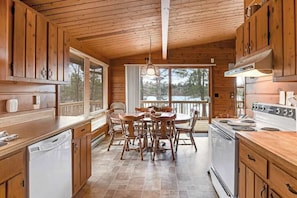 A wooden cabin interior with a dining table, chairs, a stove, and a view through the window. - Cozy lakefront cabin in the heart of Wisconsin's Northwoods with canoe & kayak (Lac Du Flambeau)