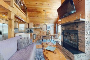 A wooden interior with a sofa, dining table, chairs, a fireplace, and a TV. - Charming Log Cabin-  Boat, fish, hike & snowmobile—minutes to lakes & trails (Friendship)