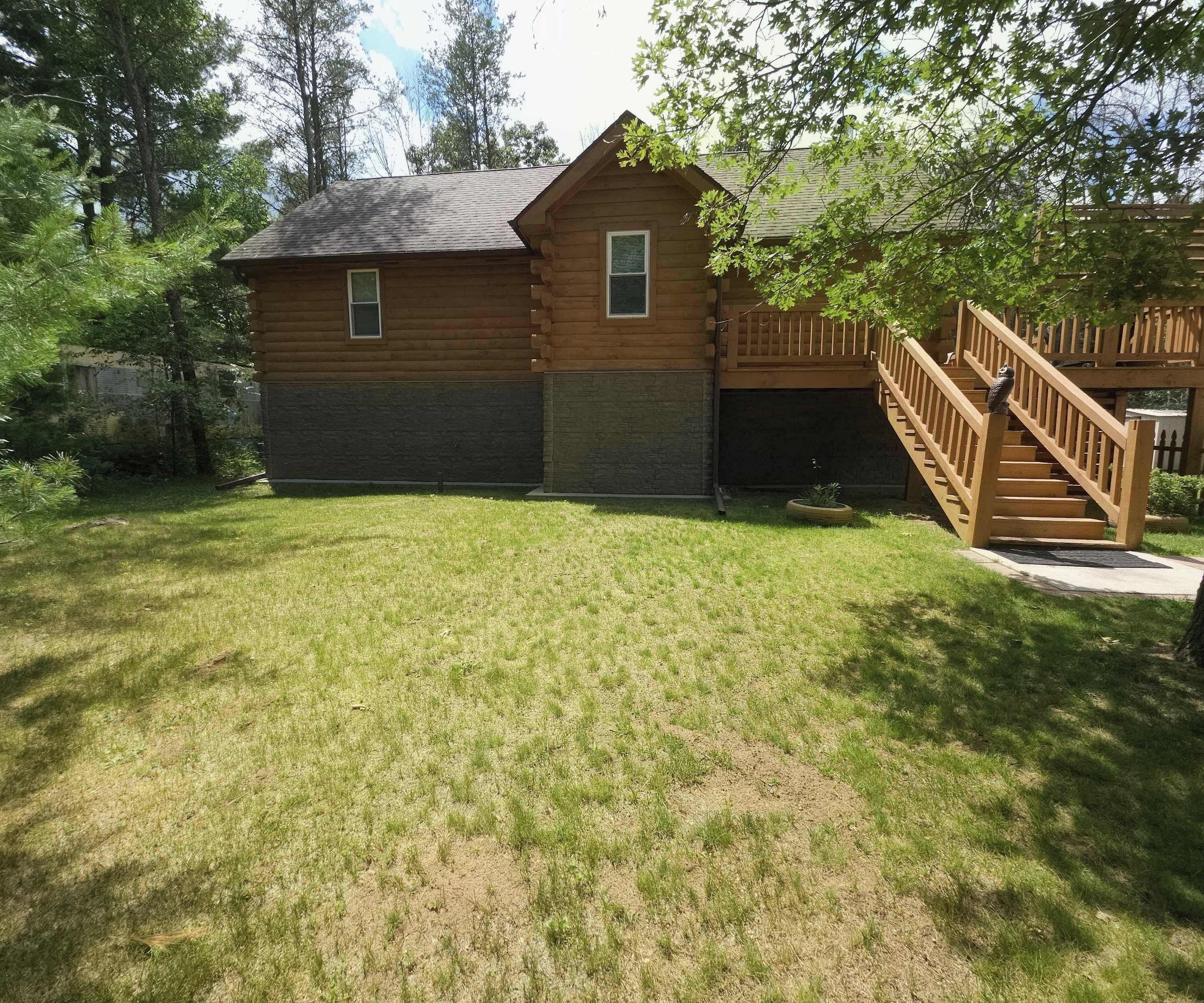 A wooden cabin with a fenced yard, a wooden staircase, and a small garden area.