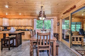 L’intérieur d’une cabane en bois comprend une table à manger, des chaises, un coin cuisine et de grandes fenêtres.