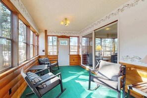 A cozy cabin with wooden walls and large windows, a green carpet, and a dining area with a table and chairs.