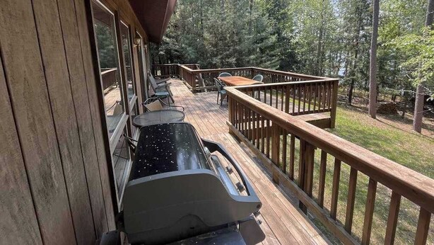Una terrassa de fusta amb una barbacoa, seients exteriors i vistes a un bosc.
