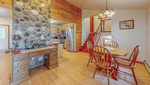 Une cuisine avec des meubles de rangement en bois, un mur en pierre, un coin repas avec des chaises en bois et un escalier.