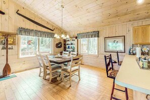 Ein Holzblock-Interieur mit Esstisch, Stühlen, einer Küchenzeile und einem großen Fenster.
