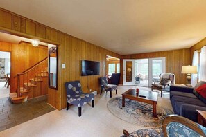 A wooden-paneled living room with a staircase, a flat-screen TV, and a sofa. - Gorgeous lakefront home with dock, sandy beach area, fireplace, huge deck & WIFI (Minocqua)