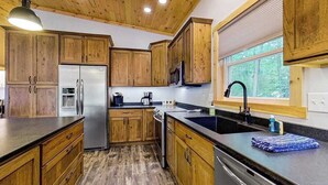 Una cocina con armarios de madera, un refrigerador de acero inoxidable, un microondas y una ventana con persianas.