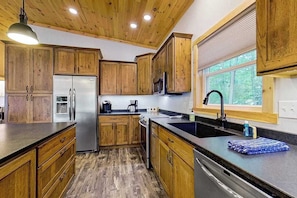 A kitchen with wooden cabinets, a stainless steel refrigerator, a microwave, and a window with blinds. - Dog-friendly lakefront hideaway with docks, firepit, fireplace & W/D (Minocqua)