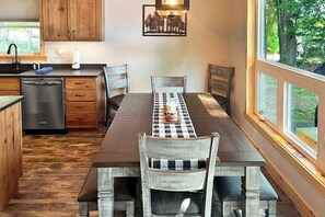 Un comedor con mantel a cuadros, sillas de madera y vistas al exterior a través de amplios ventanales.