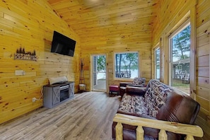 A wooden cabin interior with a fireplace, sofa, and large windows. - Dog-friendly lakefront hideaway with docks, firepit, fireplace & W/D (Minocqua)
