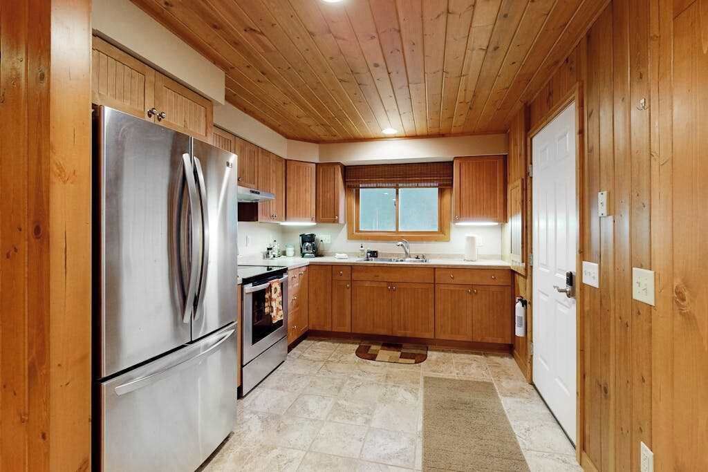 A kitchen with wooden cabinets, stainless steel appliances, a window, and a tiled floor.