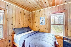 A wooden-paneled room with a bed, a window, and a painting on the wall.