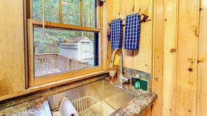 A wooden cabin kitchen with a window, sink, and hanging towels. - Tranquil & serene cabin getaway w/ large patio, fire pit, & lovely nature views (Rhinelander)