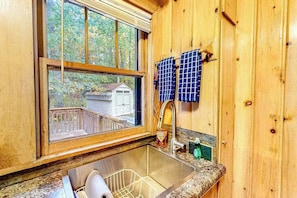 A wooden cabin kitchen with a window, sink, and hanging towels.