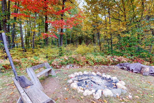 A forested campsite with a fire pit, a wooden bench, and a tarp-covered area.