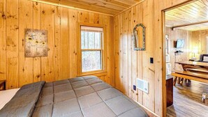 A wooden cabin interior with a bed, a window, and a mirror on the wall. - Tranquil & serene cabin getaway w/ large patio, fire pit, & lovely nature views (Rhinelander)