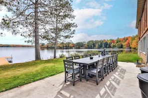 An outdoor dining area with a table and chairs, a tree, and a view of a lake and forest.