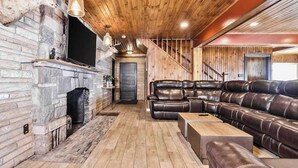 Ein gemütliches Wohnzimmer mit Kamin, Ledersofa, Holzdielen und einer Treppe.