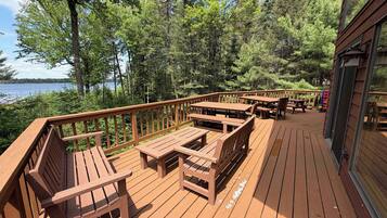 Une terrasse en bois, dotée de bancs et de tables, qui offre une vue sur un lac et est entourée d’arbres.