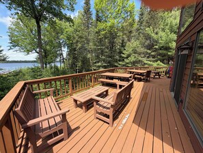 A wooden deck with benches and tables, overlooking a lake and surrounded by trees.