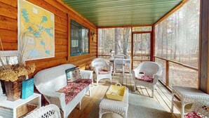 A log cabin with a porch, wicker furniture, a map on the wall, and a view of trees. - Riverfront home on the Manitowish Riverway w/ fire pit, kayaks & boat house (Manitowish Waters)