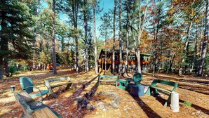 A rustic cabin surrounded by tall trees, with a clear sky. - Riverfront home on the Manitowish Riverway w/ fire pit, kayaks & boat house (Manitowish Waters)