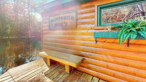 A wooden cabin with a bench and a sign reading 'MANTOWISH MIKE'S' by a body of water. - Riverfront home on the Manitowish Riverway w/ fire pit, kayaks & boat house (Manitowish Waters)