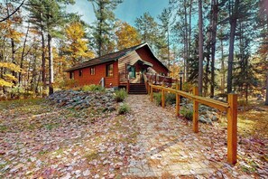 Een houten hut met terras, een trap naar de ingang, omgeven door bomen en een pad van stenen.
