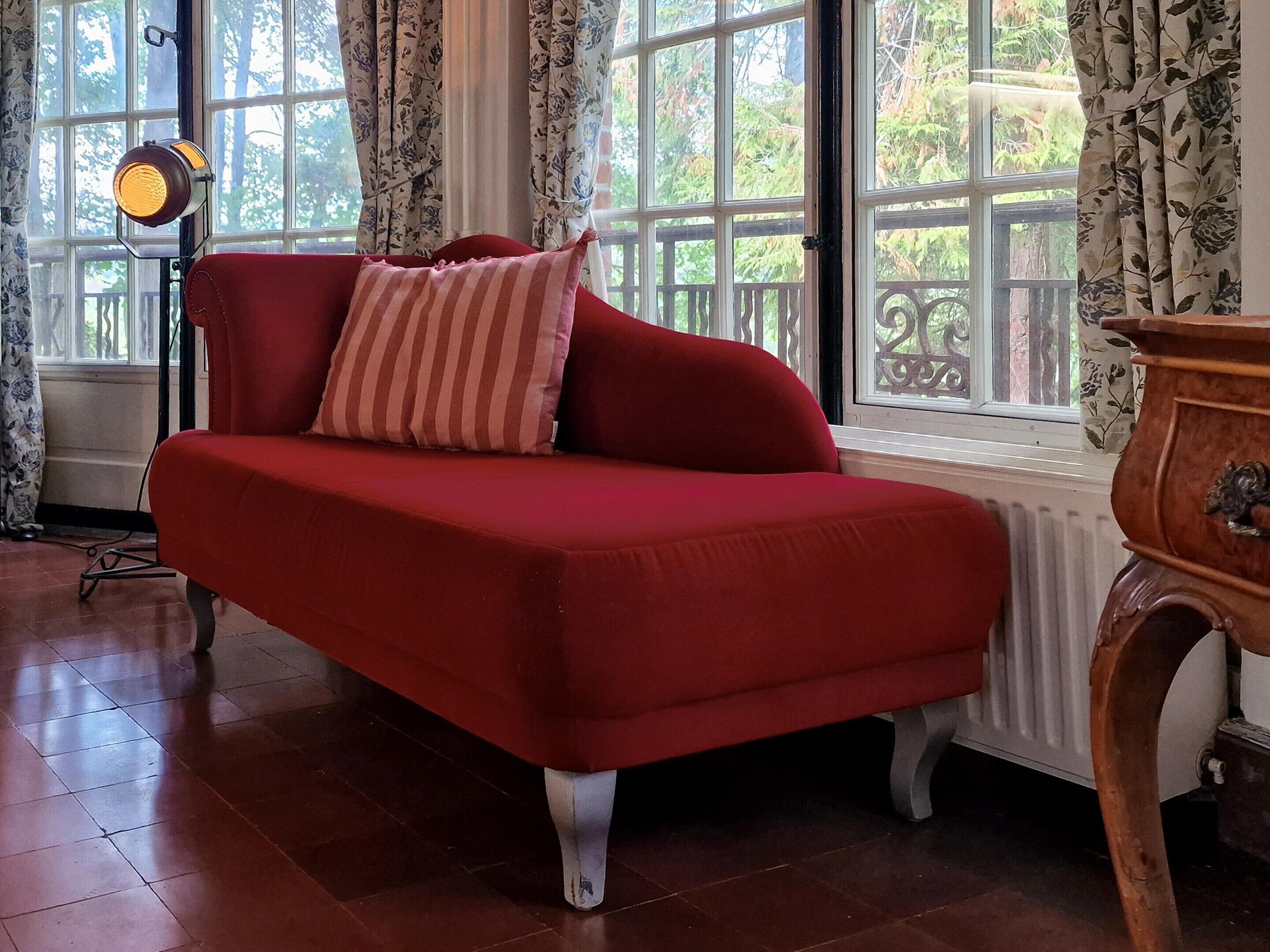 Um sofá vermelho com almofadas listradas, um radiador e uma janela com cortinas.