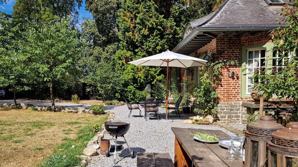 Een terras met een barbecue, buitenmeubels en een pad van stenen.