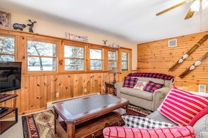 A cozy room with wooden walls, a sofa with plaid cushions, a coffee table, and a television. - Lakefront, dog-friendly home with beach access, kayaks and firepit (Phelps)