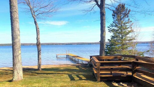 Une vue sur le lac, avec une jetée en bois qui s’avance dans l’eau, entourée d’arbres et d’une zone herbeuse.