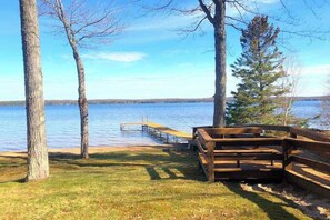 A lakeside view with a wooden dock extending into the water, surrounded by trees and a grassy area.