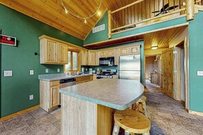 A kitchen with wooden cabinets, a central island, and a dining area with stools. - Three Cozy Cabins located on the Turtle Flambeau Flowage, great for all seasons! (Mercer)