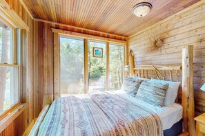 A wooden cabin interior with a bed, large windows, and a ceiling light. - Riverside Home with Firepit,  Gas Grill,  and Washer/Dryer (Manitowish Waters)