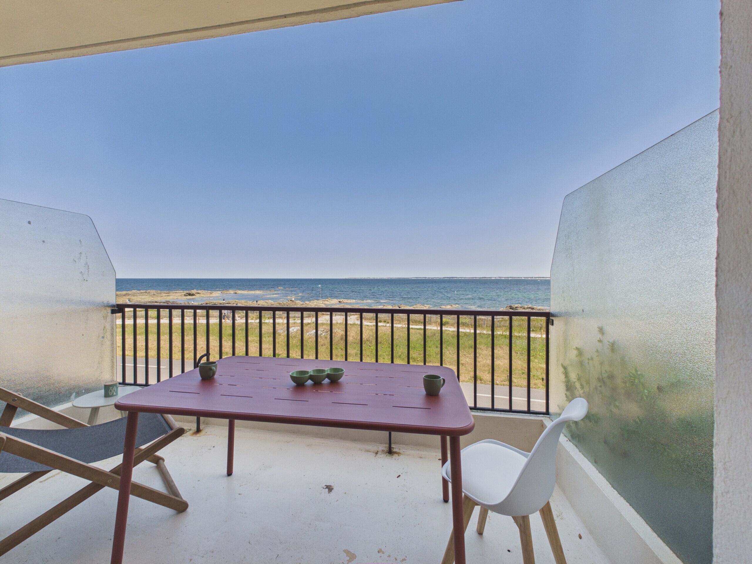 Ein Balkon mit Tisch und Stühlen mit Blick auf einen Strand.
