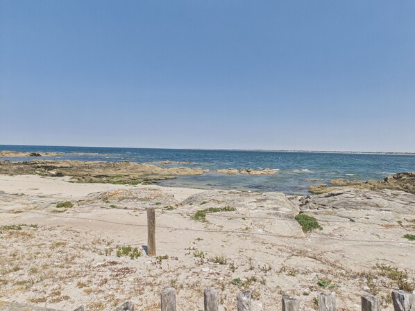 A rocky beach with clear blue water and a wooden fence in the foreground. - Apartment with sea view 100m from the beach (Le Croisic)
