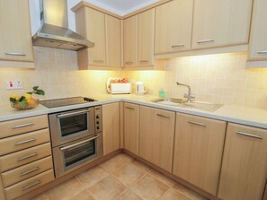 A modern kitchen with wooden cabinets, a built-in oven, a toaster, and a sink. - Harbourside (Porthmadog)