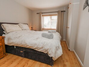 A bedroom with a bed, bedside tables, a window with curtains, and a wardrobe. - September Cottage (Weymouth)