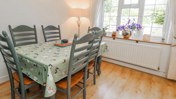 A dining area with a table set for four, chairs, a lamp, and a window with curtains. - September Cottage (Weymouth)