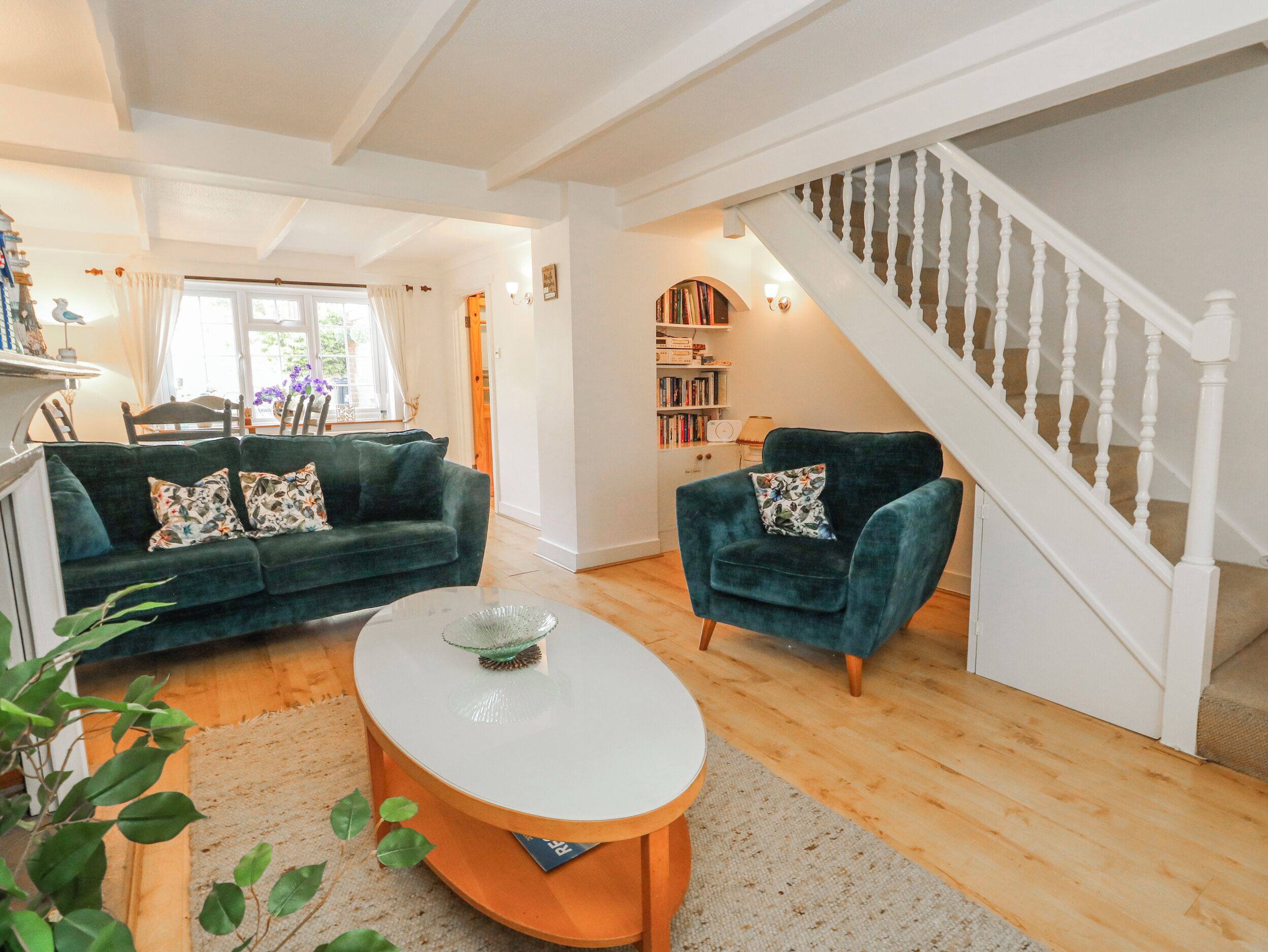 A living room with a sofa, armchair, coffee table, staircase, bookshelf, and a dining area with chairs and a table.