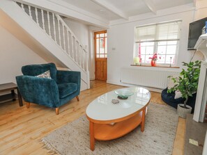 Ein Wohnzimmer mit blauem Sessel, einem Glastisch, einer Treppe, einem Fenster mit Jalousien und einer Heizung.