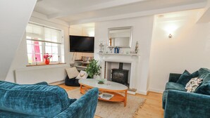 A living room with a fireplace, a television, and two blue sofas. - September Cottage (Weymouth)