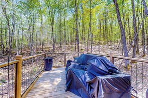 Eine Holzterrasse mit überdachter Sitzgruppe, umgeben von einem Metallgeländer und Bäumen.