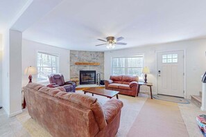 Ein Wohnzimmer mit Kamin aus Stein, zwei Ledersofas, einem Couchtisch und einem Deckenventilator.